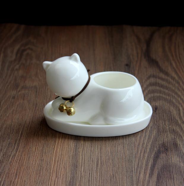 White ceramic cat-shaped container with a small bell on a wooden surface