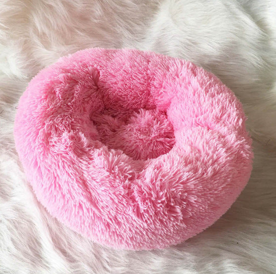 Pink fluffy donut-shaped pet bed on a white fur surface