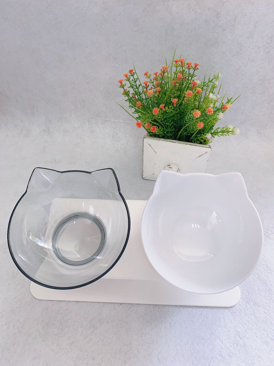 Cat-shaped feeding station with two bowls and a small plant on a light gray background