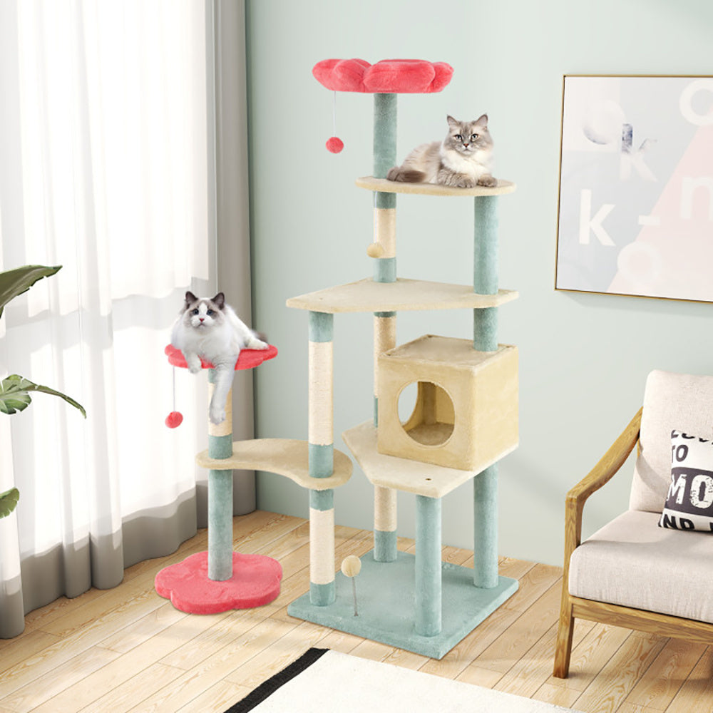 Cat tree with multiple levels and a cat sitting on top in a room with a couch and plant.