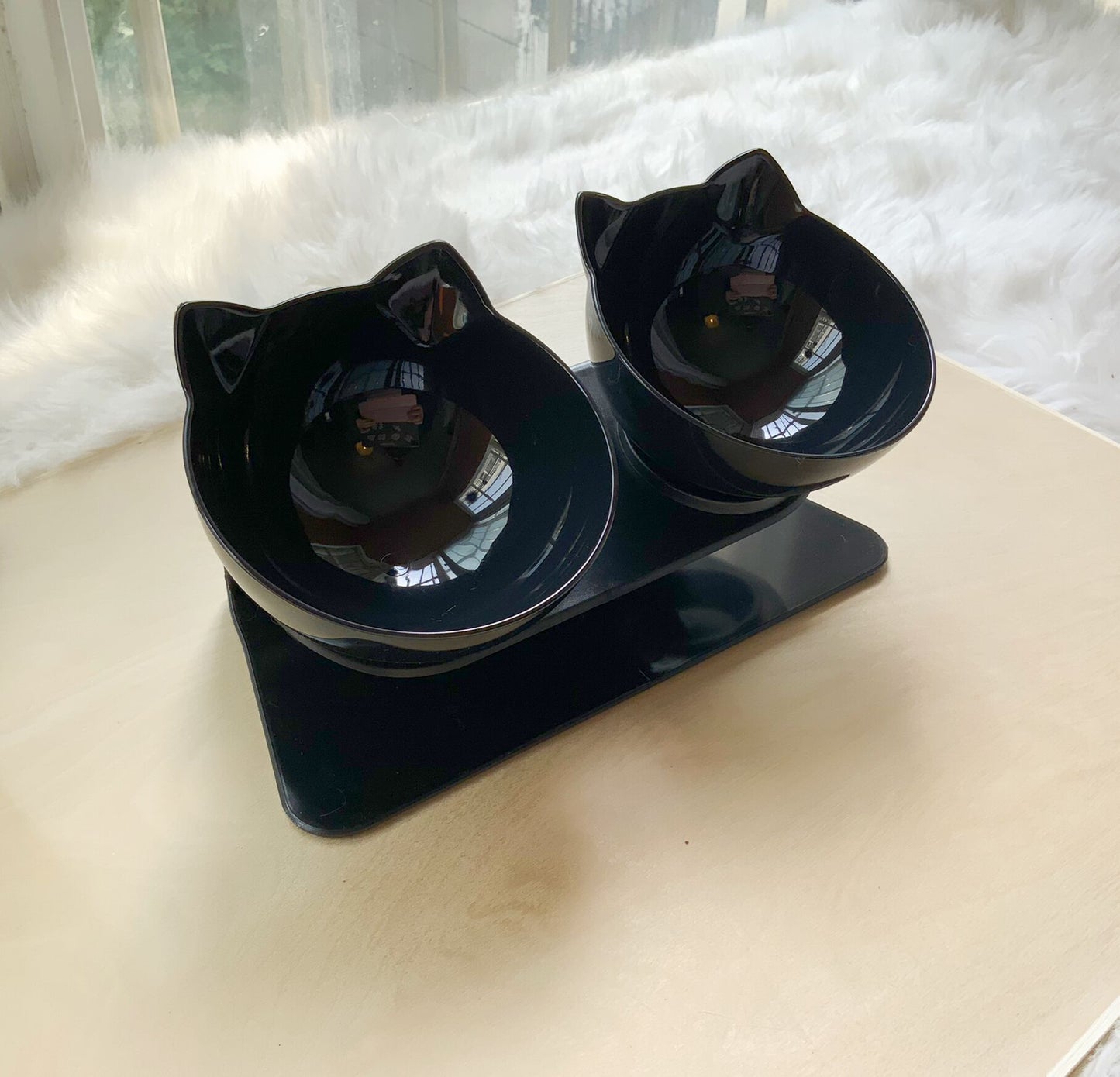 Black cat-shaped double bowl feeder on a light surface with a blurred background