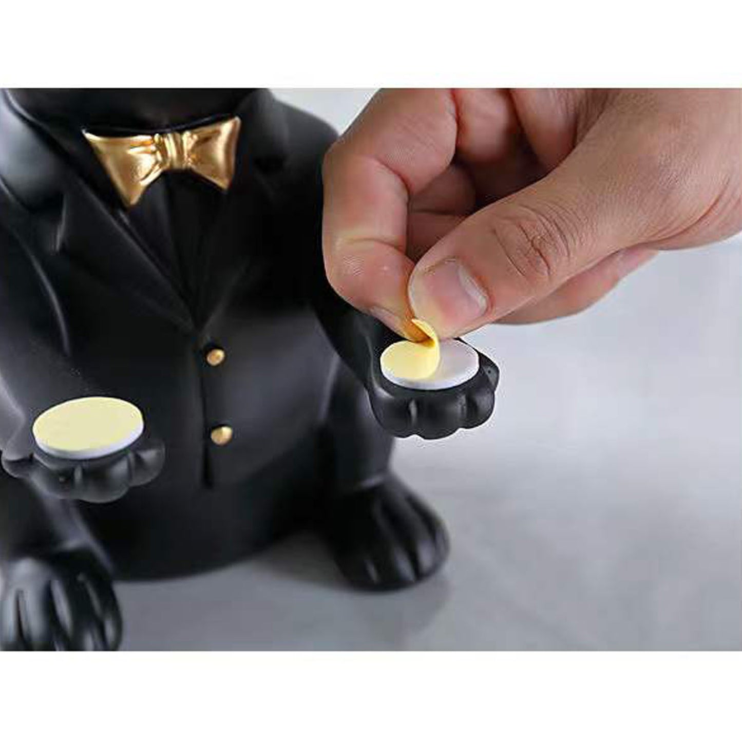 Black dog figurine in a suit with a hand placing a coin into its mouth on a white background
