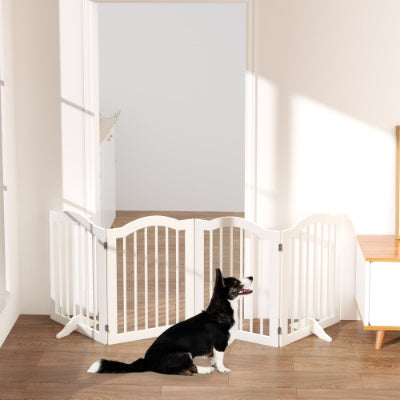 Dog standing in front of a white pet gate in a room with wooden flooring and a light-colored wall.
