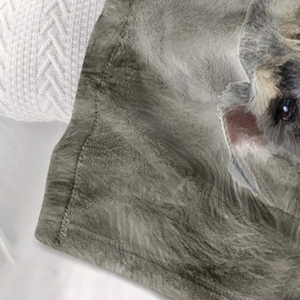 Close-up of a gray dog lying on a textured blanket with a white pillow.