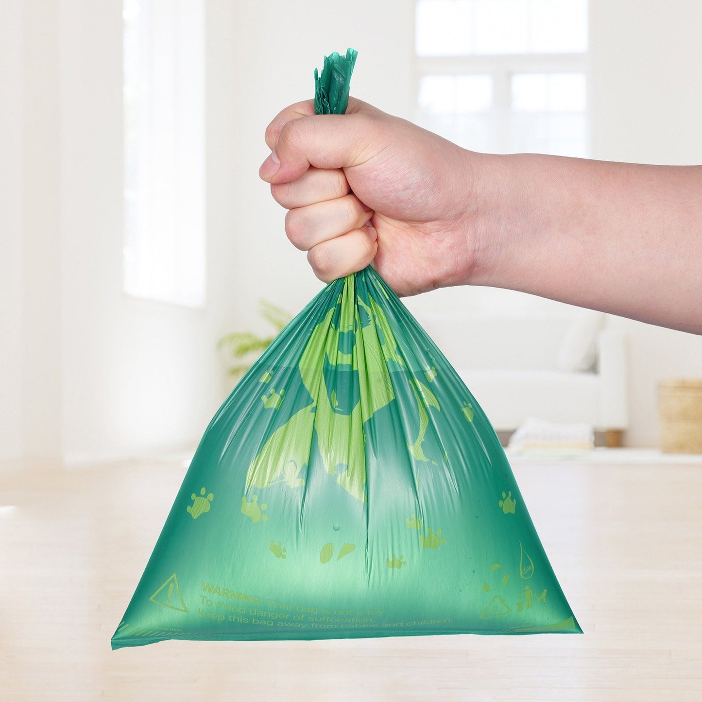 Hand holding a green plastic bag with paw prints on a blurred indoor background