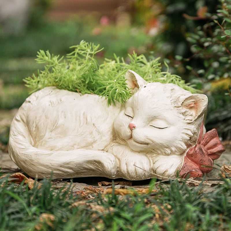 White cat-shaped planter with a pink bow in a garden setting