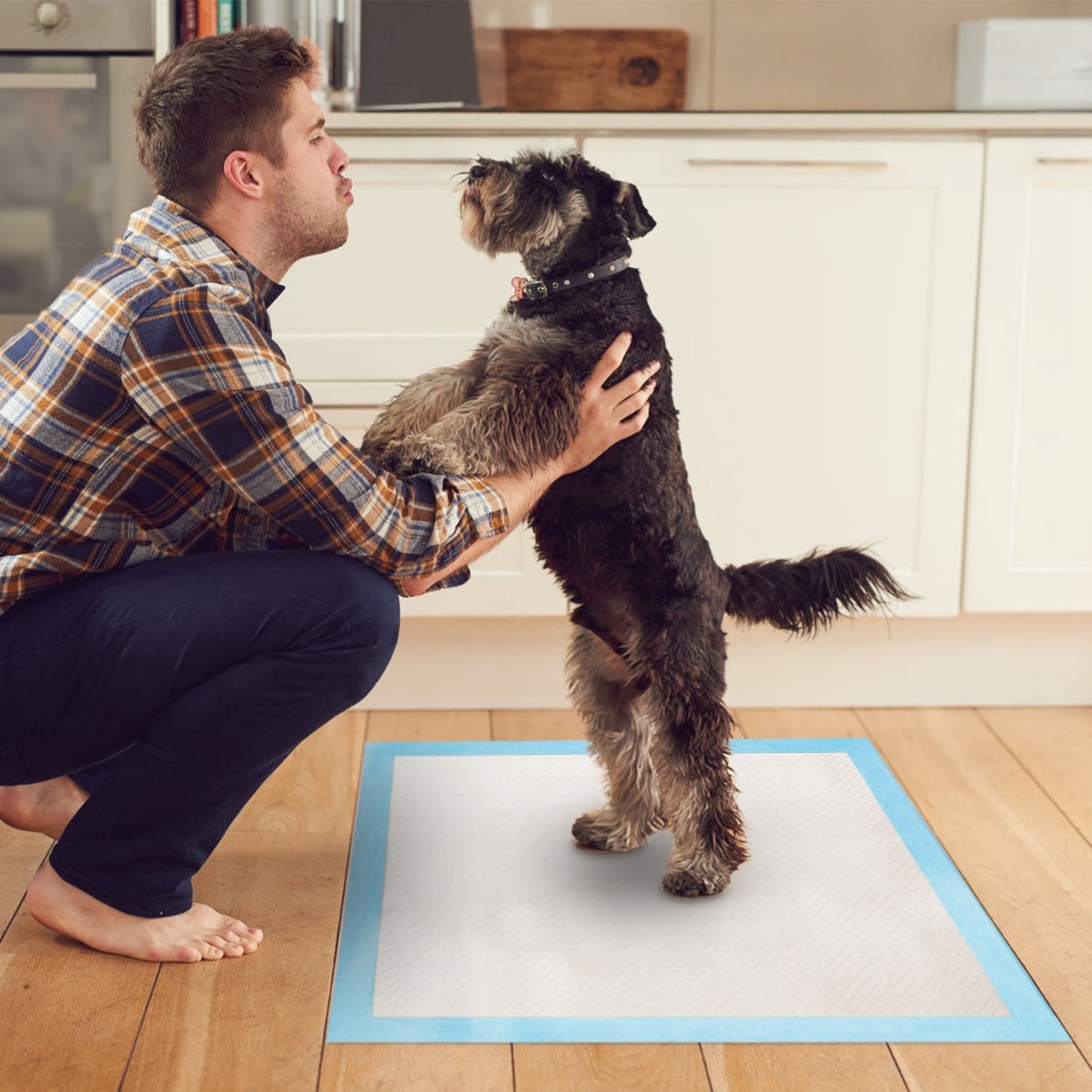 Man petting a dog on a wooden floor with a white training pad.