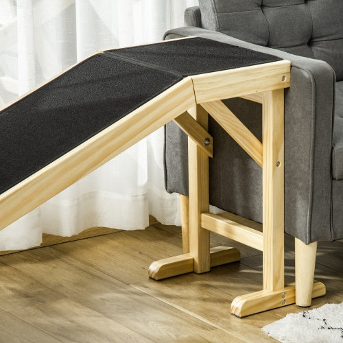 Wooden pet ramp with black mat against a gray sofa on a wooden floor.