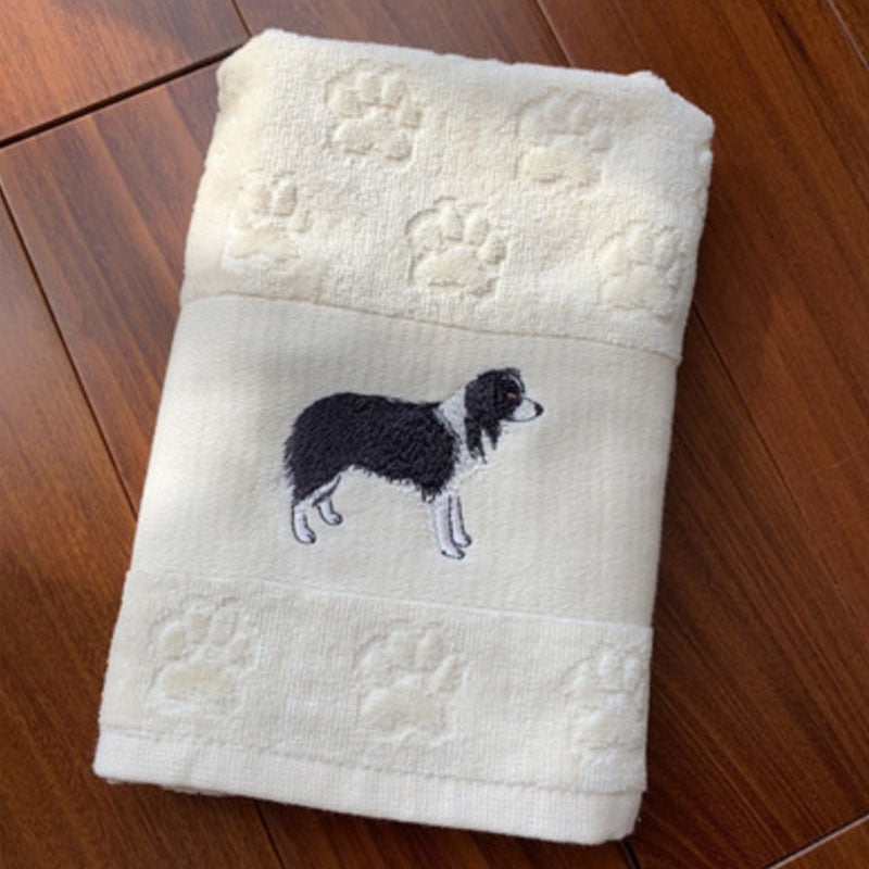 Folded white towel with embroidered black and white dog design on a wooden surface