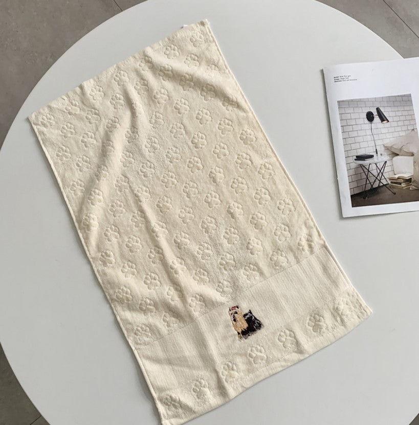 Beige embroidered towel on a white surface with a magazine in the background