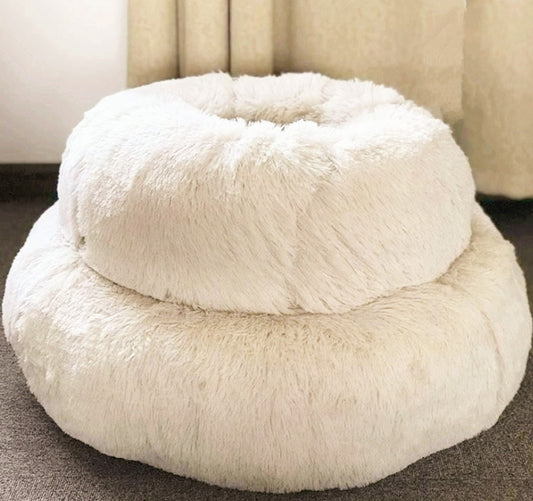 White fluffy donut-shaped pet bed on a carpeted floor.
