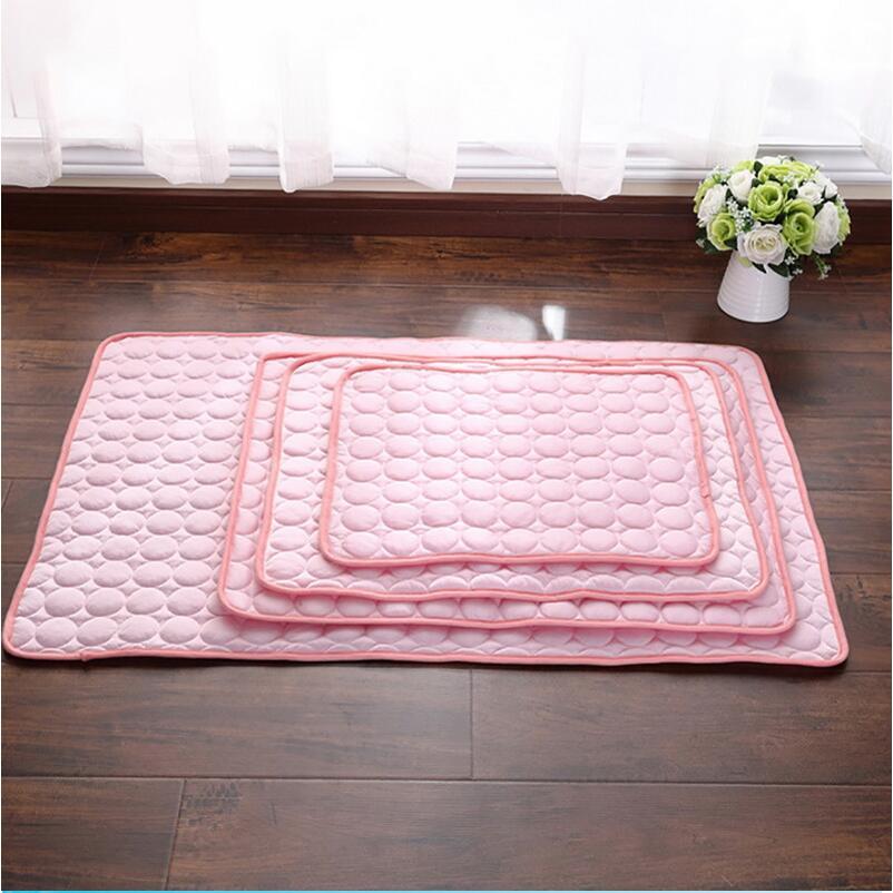 Set of pink quilted self-cooling pet pad on a wooden floor with a vase of flowers in the background.