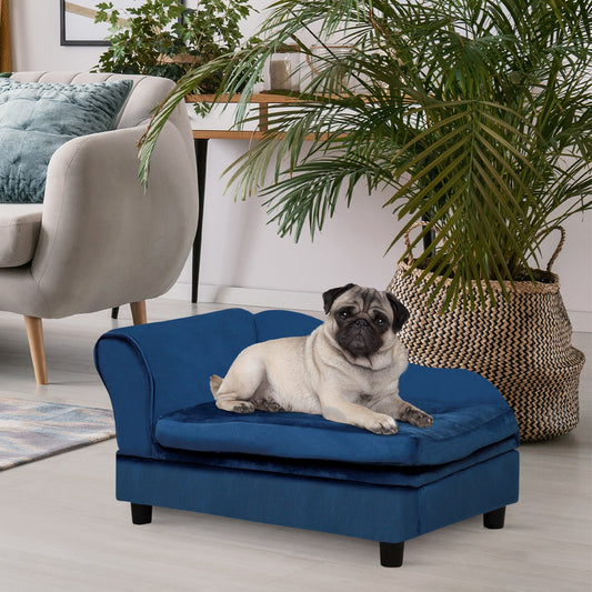 Dog lying on a blue pet bed in a living room with a plant and chair in the background.