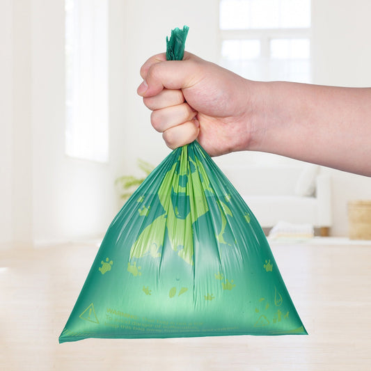 Hand holding a green plastic bag with paw prints on a blurred indoor background