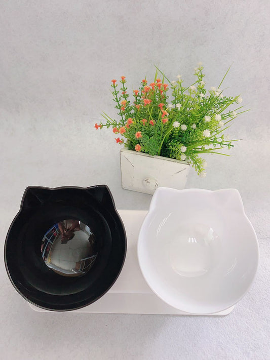 Black and white cat-shaped bowls with a small potted plant on a light gray background