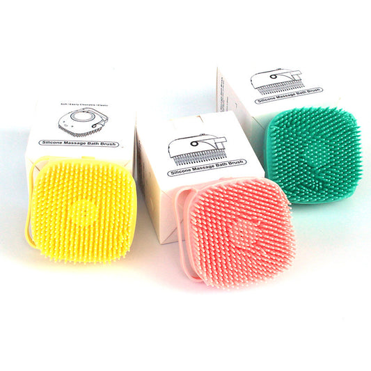 Three silicone massage bath brushes in yellow, pink, and green with their packaging on a white background.