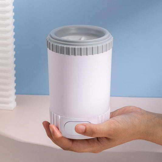 Hand holding a cylindrical white and gray dog paw cleaning device against a light blue background