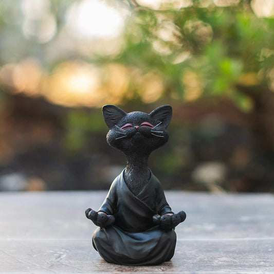 Black cat figurine in a meditative pose on a wooden surface with a blurred natural background