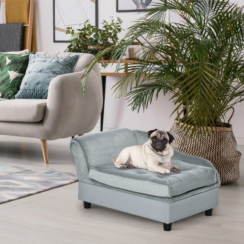 Dog lying on a light gray pet bed in a living room with a plant and sofa in the background.