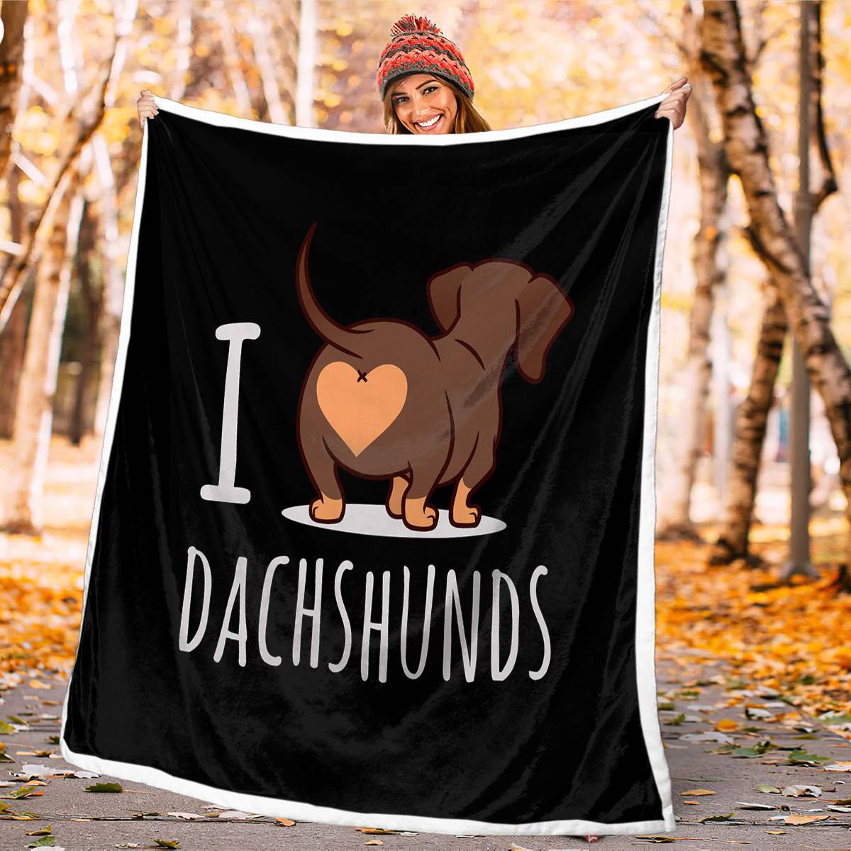Person holding a black blanket with a dachshund design and 'I love dachshunds' text in an autumn setting.